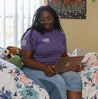 a student sits on her bed with a laptop